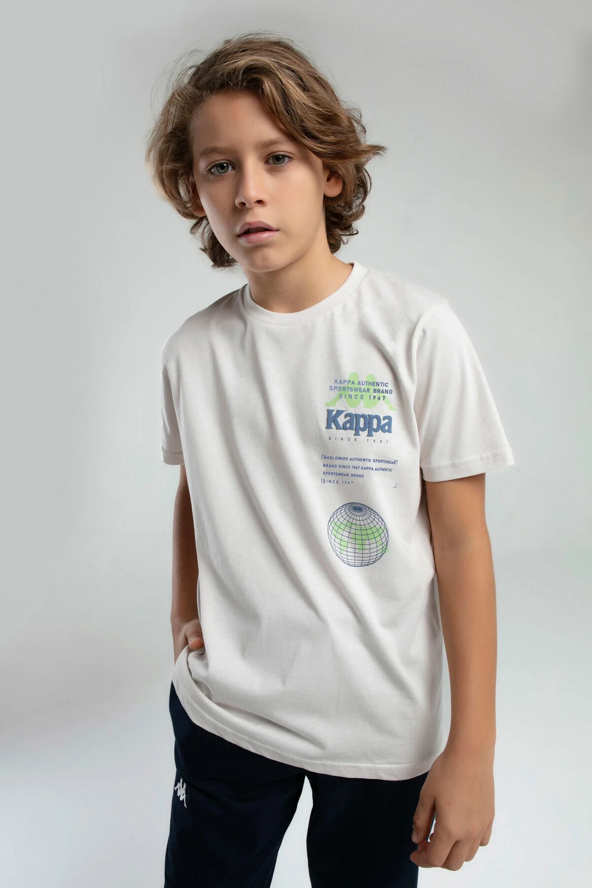 Kappa Erkek Çocuk Krem T-Shirt, beyaz zeminde model giyim, marka logosu ve küre deseni, çocuk giyim kategorisi