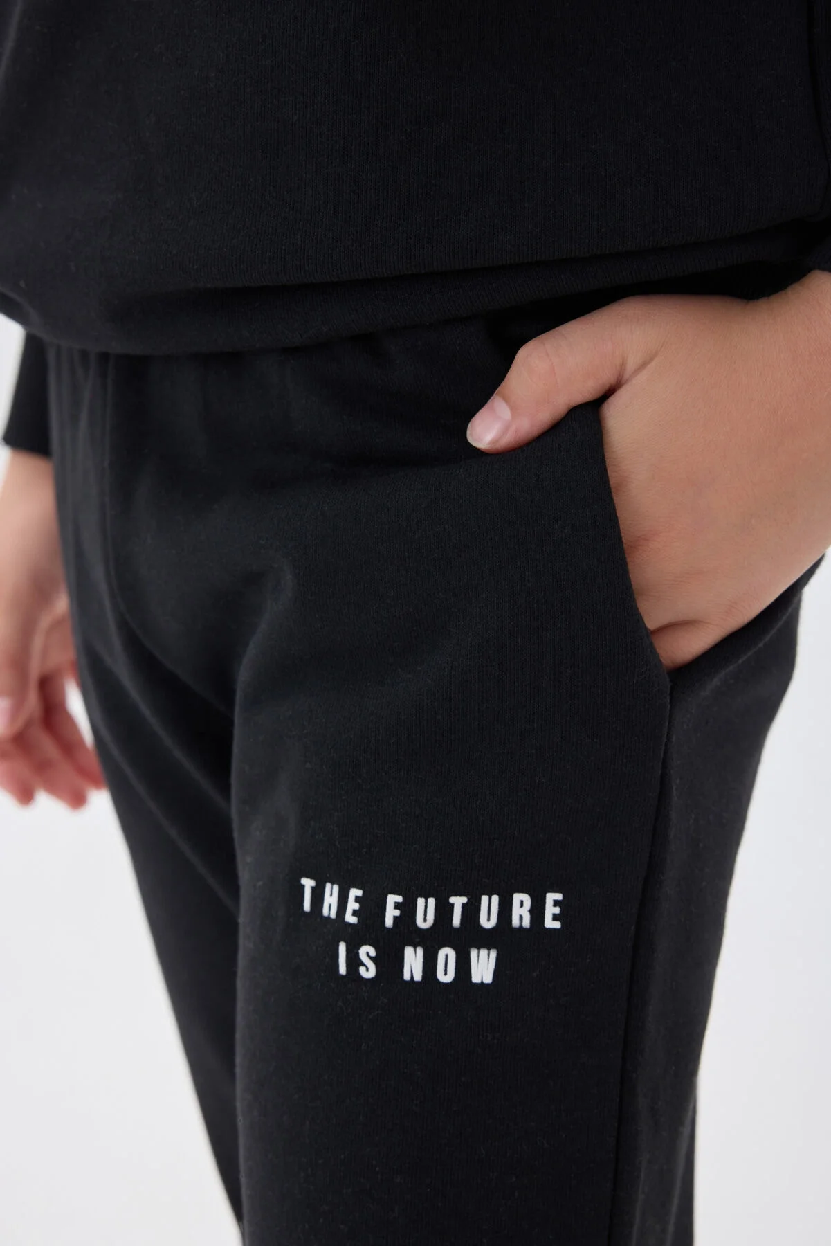 Siyah erkek çocuk eşofman takımı, Arnetta markası, kapüşonlu üst ve pantolon, 'The Future is Now' yazısı, beyaz spor ayakkabılarla model