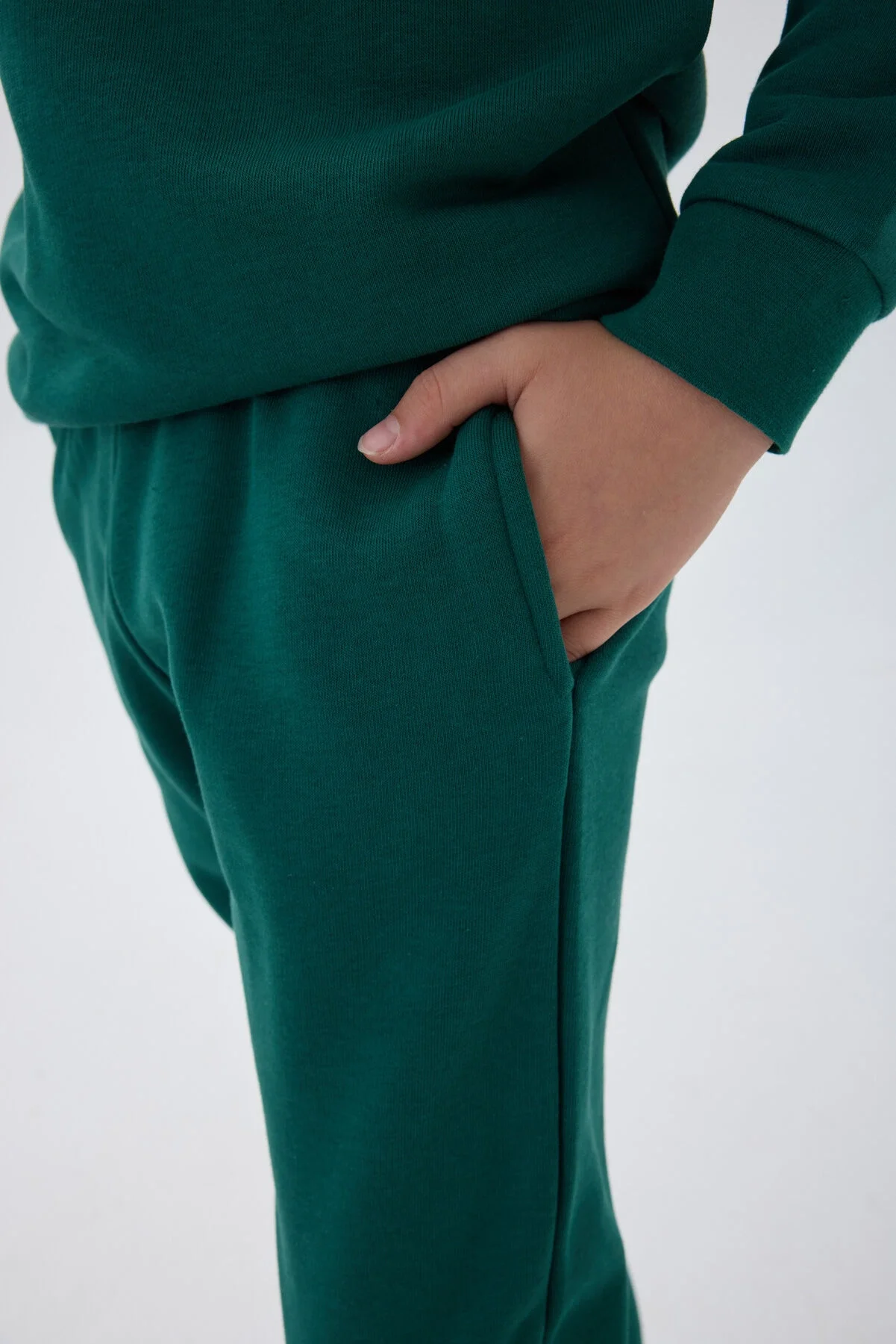 Yeşil erkek çocuk eşofman takımı, Arnetta markası, uzun kollu sweatshirt ve pantolon, beyaz ayakkabıyla model pozisyonu