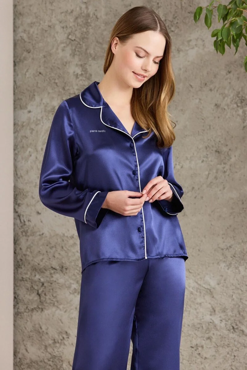 Saten biyeli lacivert pijama takımını giyen kadın, Pierre Cardin markası, klasik yaka ve beyaz detaylarla, modern iç giyim stili