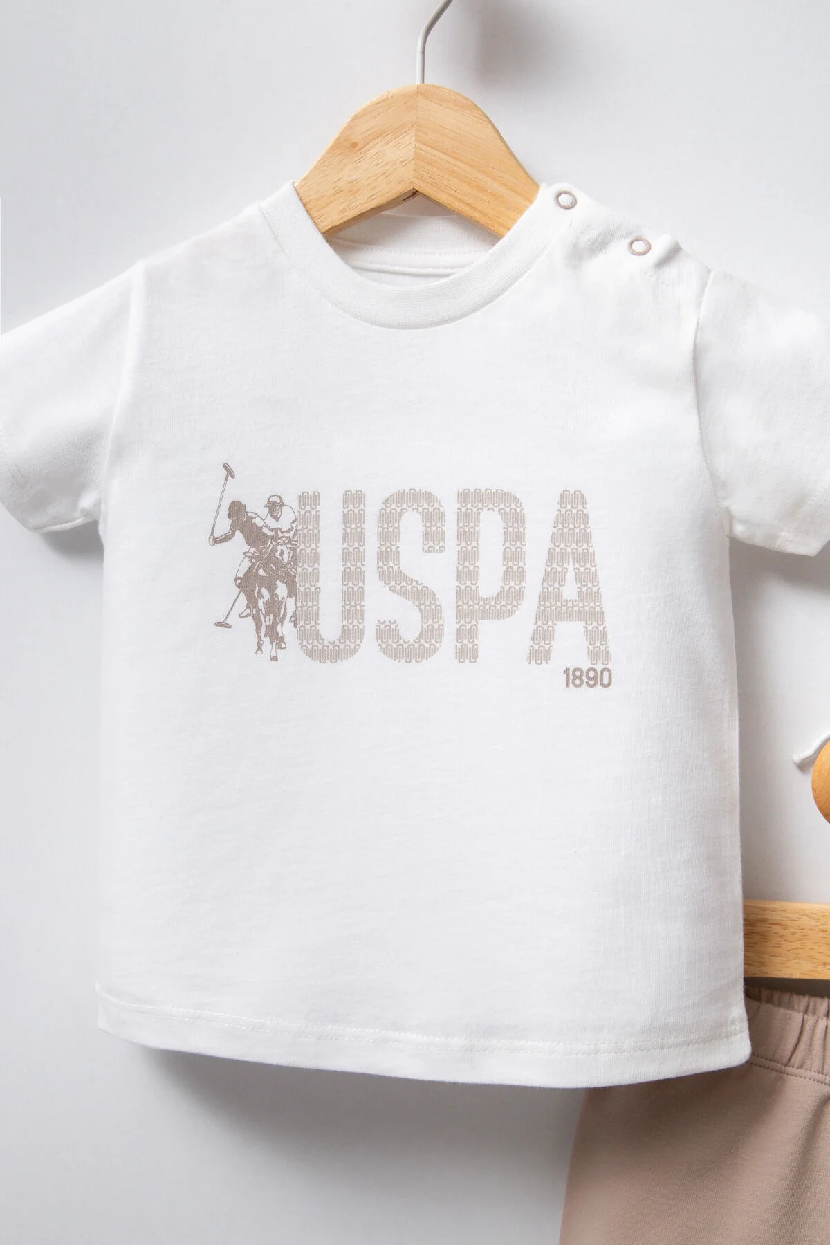 Beyaz USPA logosu ile bebek takım elbette, pastel pembe kısa pantolonlu, bebeğin giyimini gösteren ürün fotoğrafı