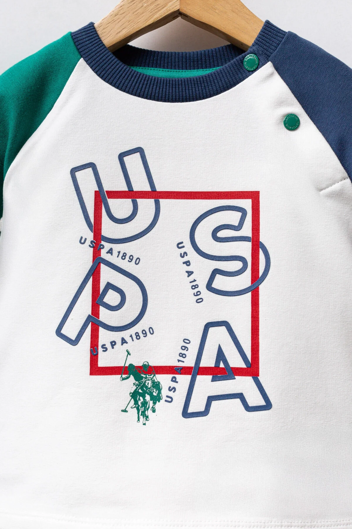 Yeşil ve mavi detaylı beyaz USA yazısı olan bebeğin takımları, kırmızı pantolonlu U.S. Polo Assn bebek takım seti