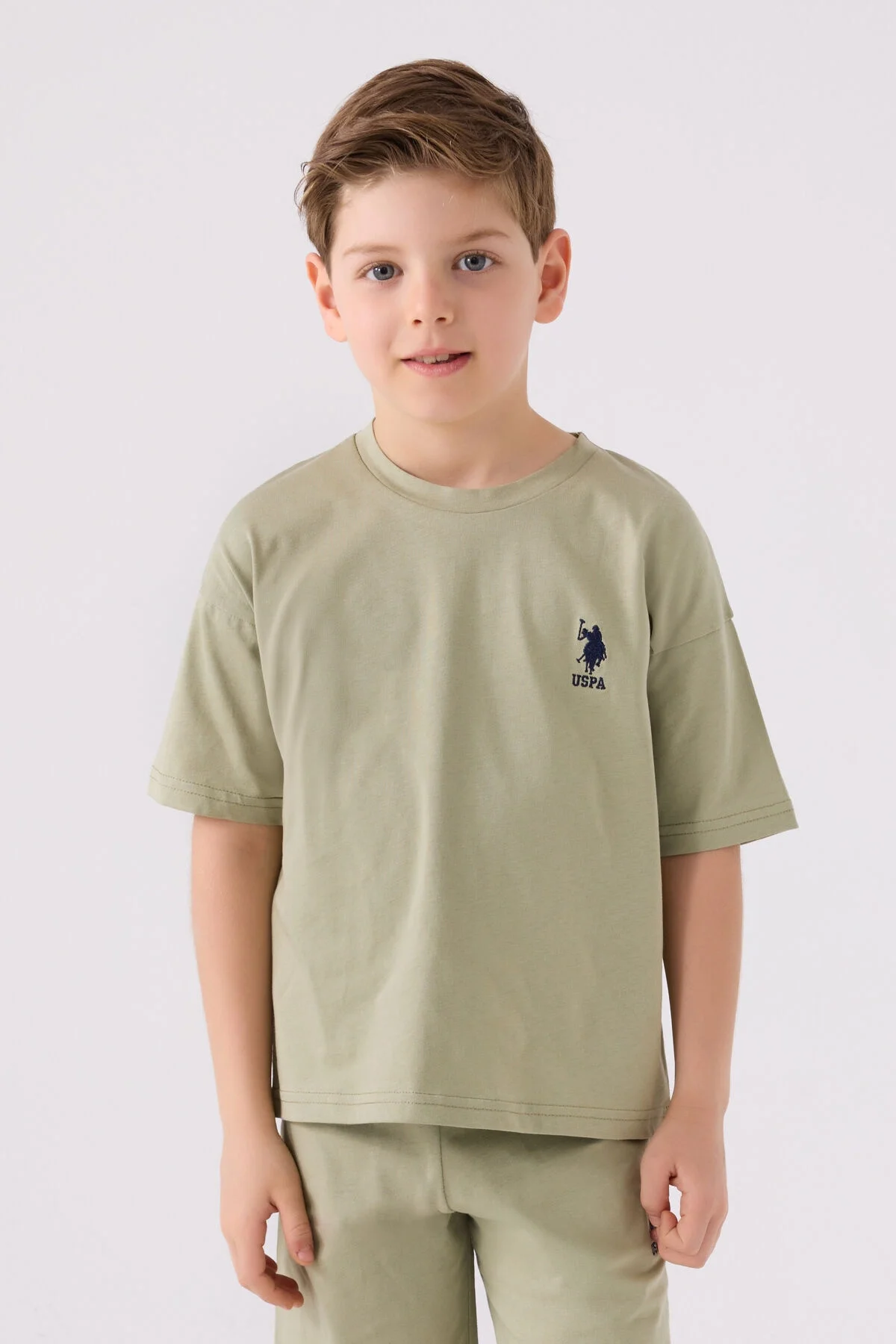 Haki renkli U.S. Polo Assn erkek çocuk Bermuda takım elbette, model ön görünümü, marka logosu ve spor ayakkabılarla takımlı