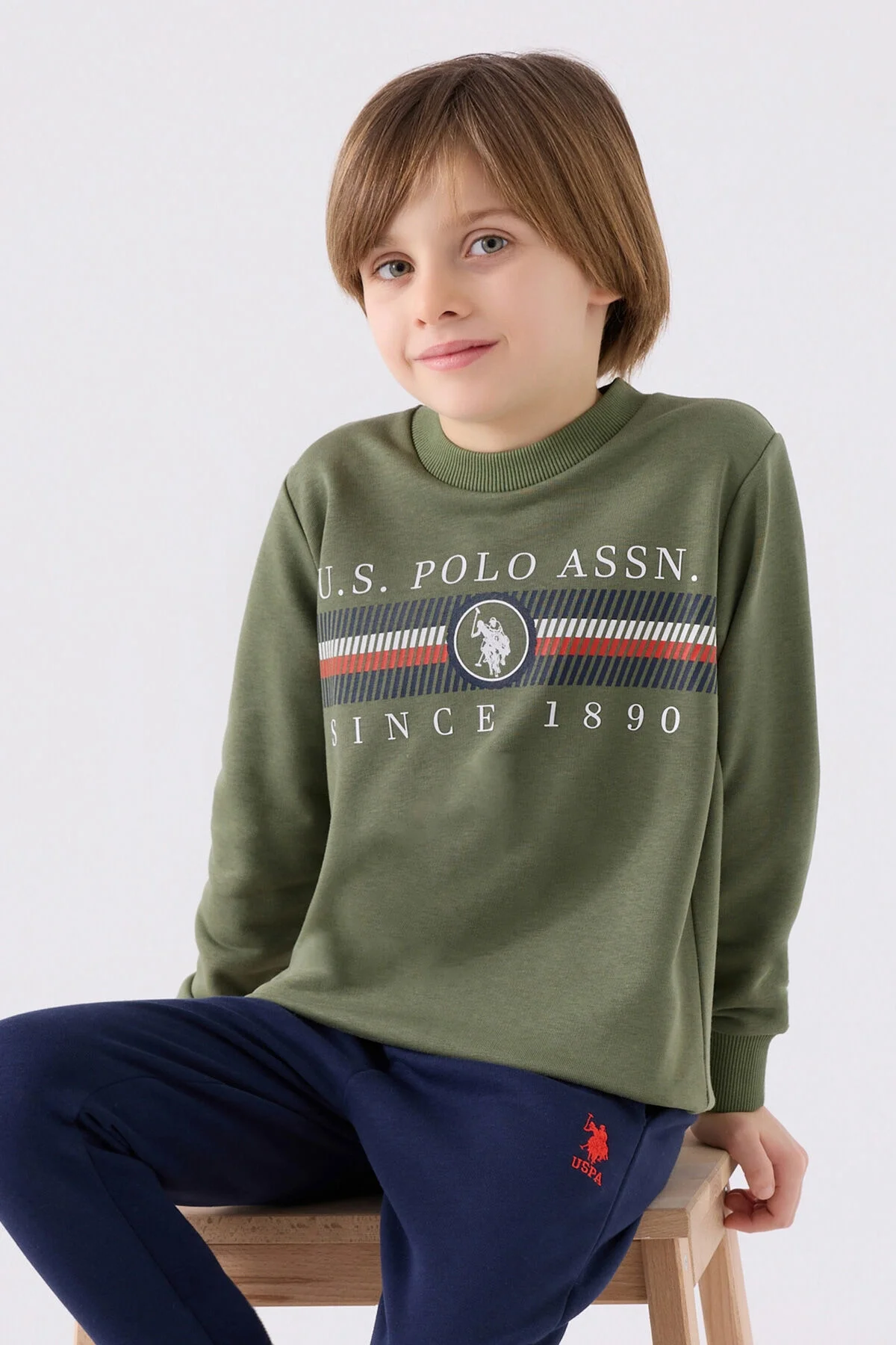 U.S. Polo Assn Erkek Çocuk Haki Eşofman Takımı, koyu mavi pantolon ve spor ayakkabıyla tamamlayıcı, marka logosu ve desenli üst detaylı