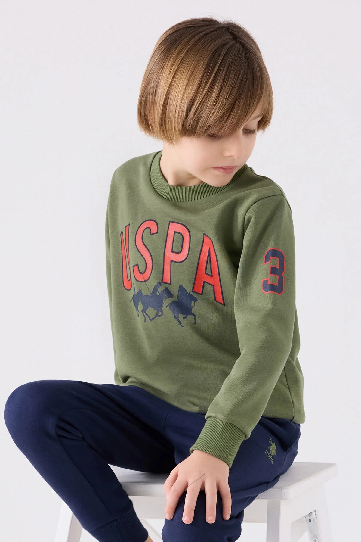 Haki renkli U.S. Polo Assn erkek çocuk eşofman takımı, kıyafet detayları ve model pozisyonu