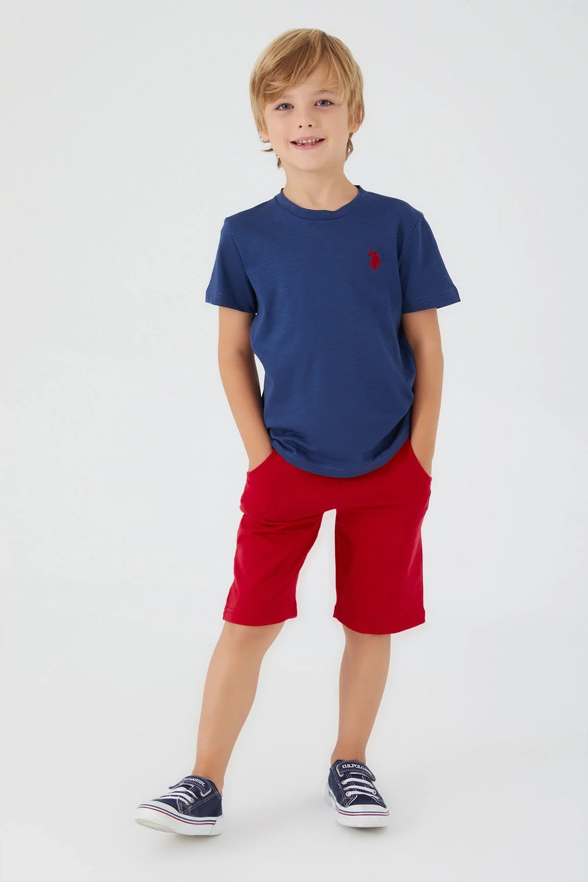 U.S. Polo Assn Erkek Çocuk Lacivert Bermuda Takım, kırmızı kısa pantolon ve mavi spor ayakkabı ile çocuk modeli
