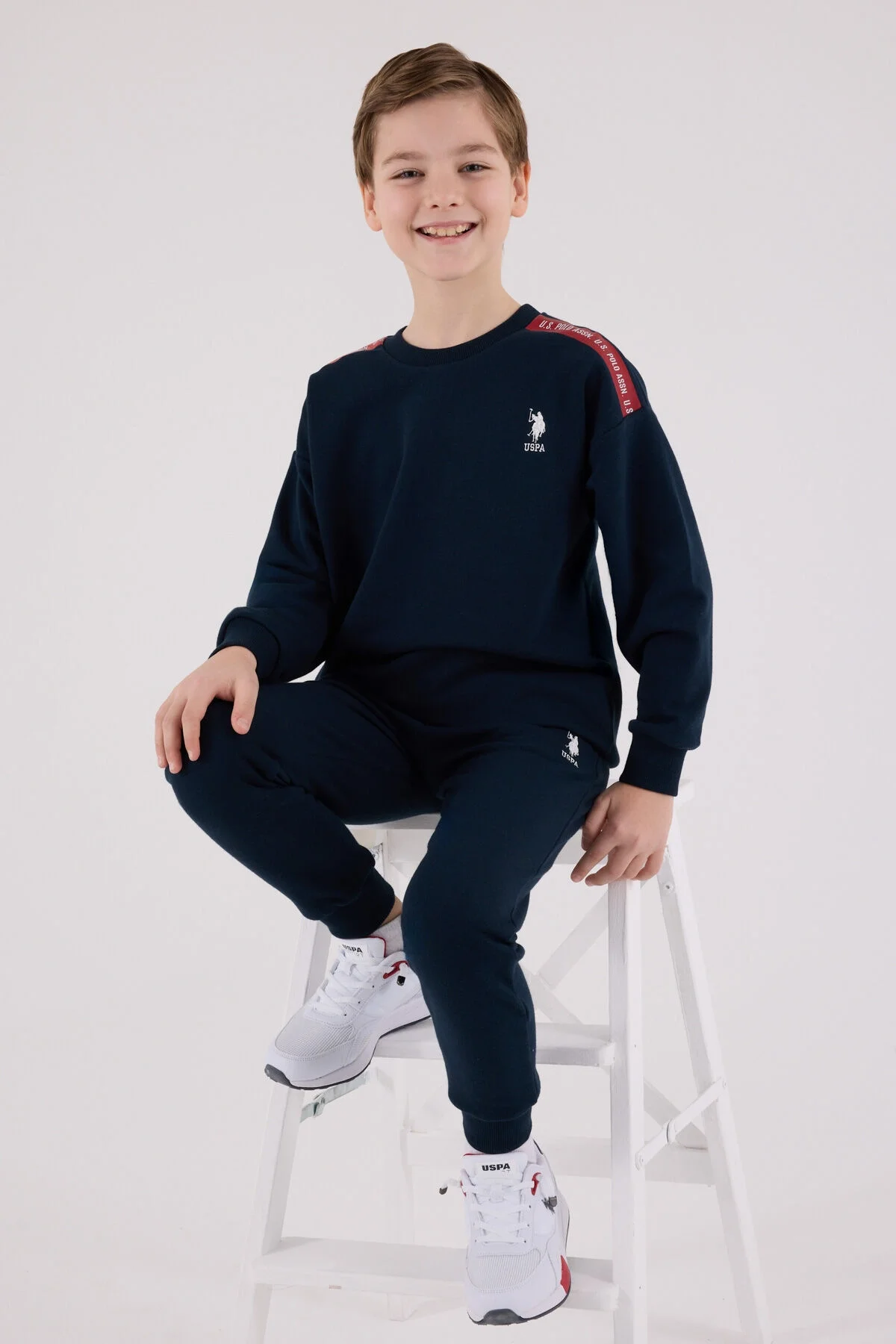 Lacivert U.S. Polo Assn erkek çocuk eşofman takımı, kolları ve pantolonunda marka logosu, beyaz spor ayakkabılarla takımlı