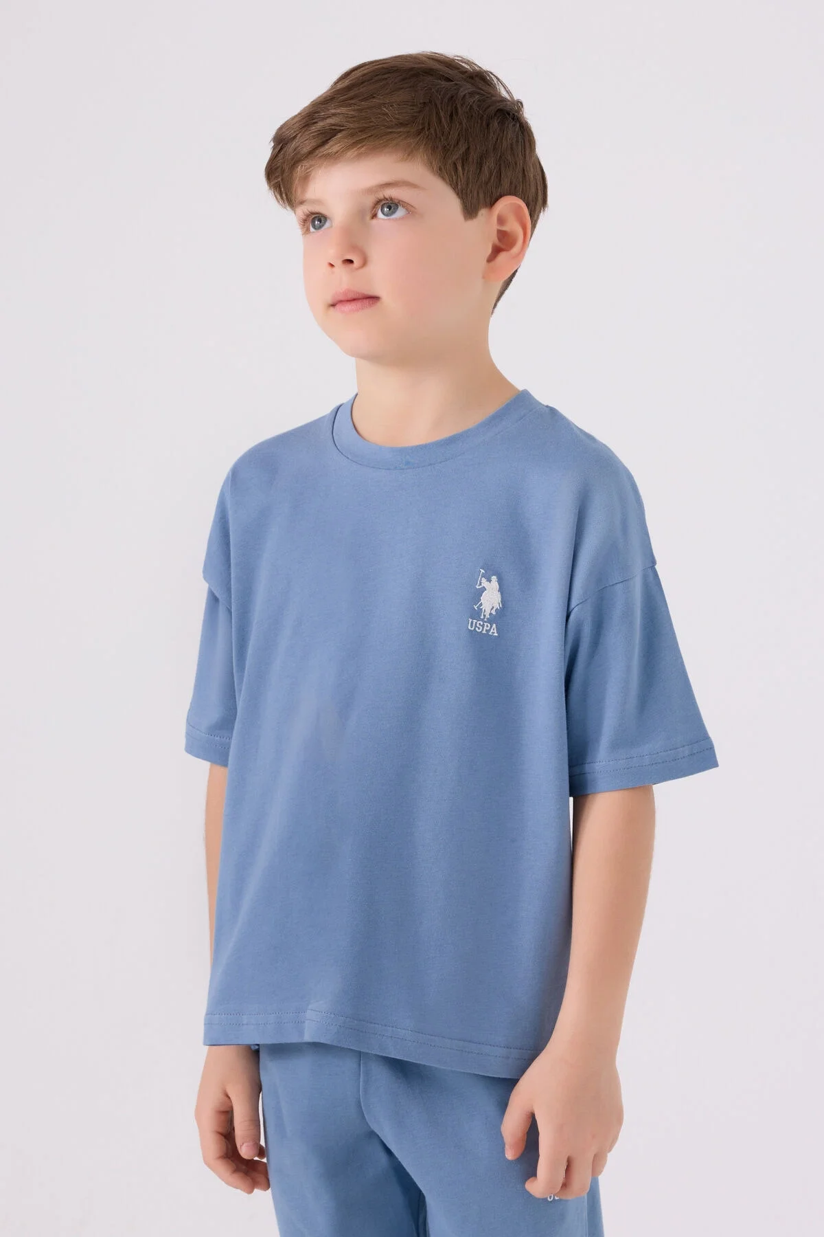 Mavi U.S. Polo Assn erkek çocuk Bermuda takım elbette, marka logosu ve model pozisyonu ile çocuk giyim detayları