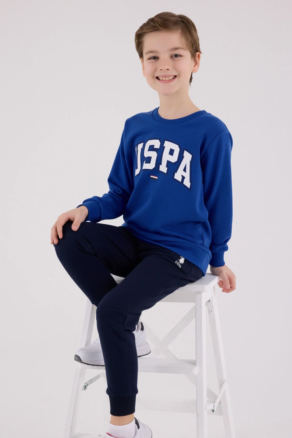 Mavi USPA erkek çocuk eşofman takımı, üstte büyük harfli logo, pantolonun ön detayı, spor stil, çocuk giyim
