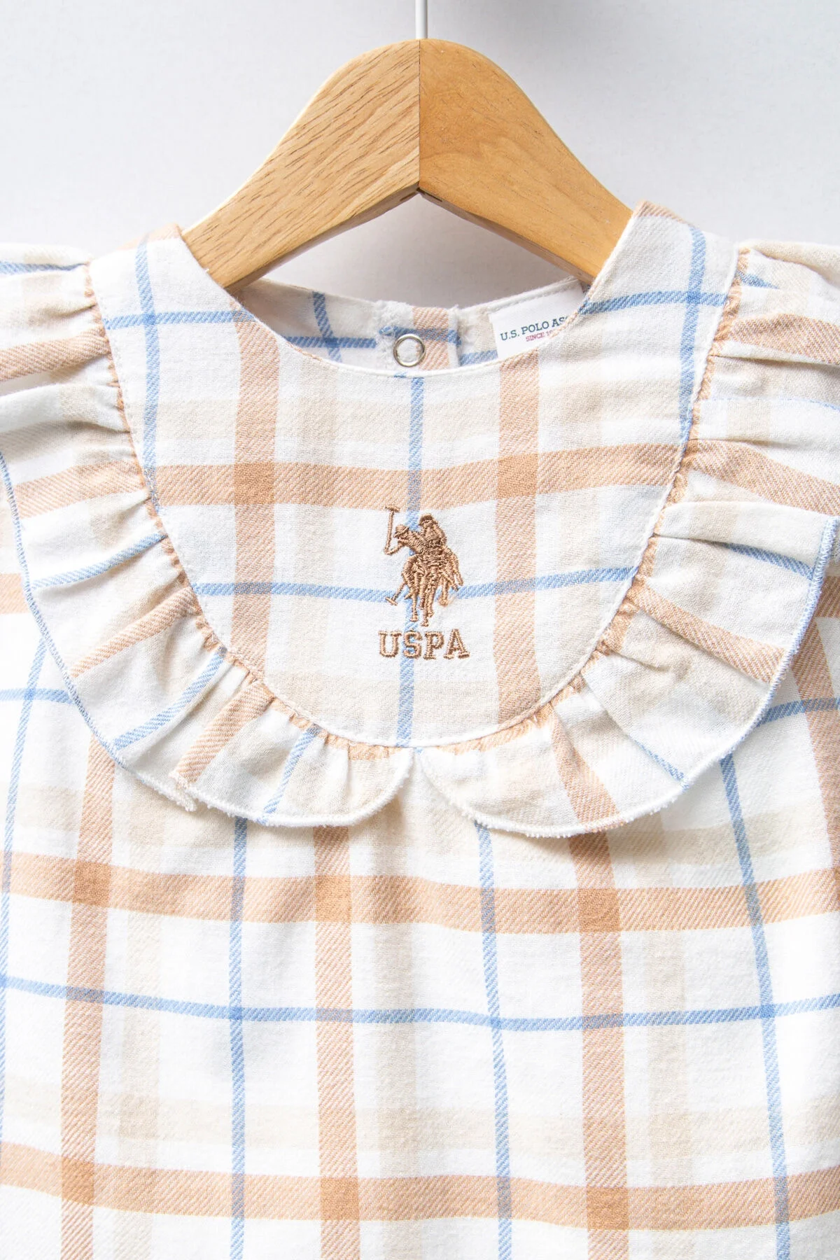 Beyaz ve krem tonlarında kareli desenli, kolları olmayan bebek elbise, U.S. Polo Assn markası, ruffled yaka, arka plan: beyaz duvar