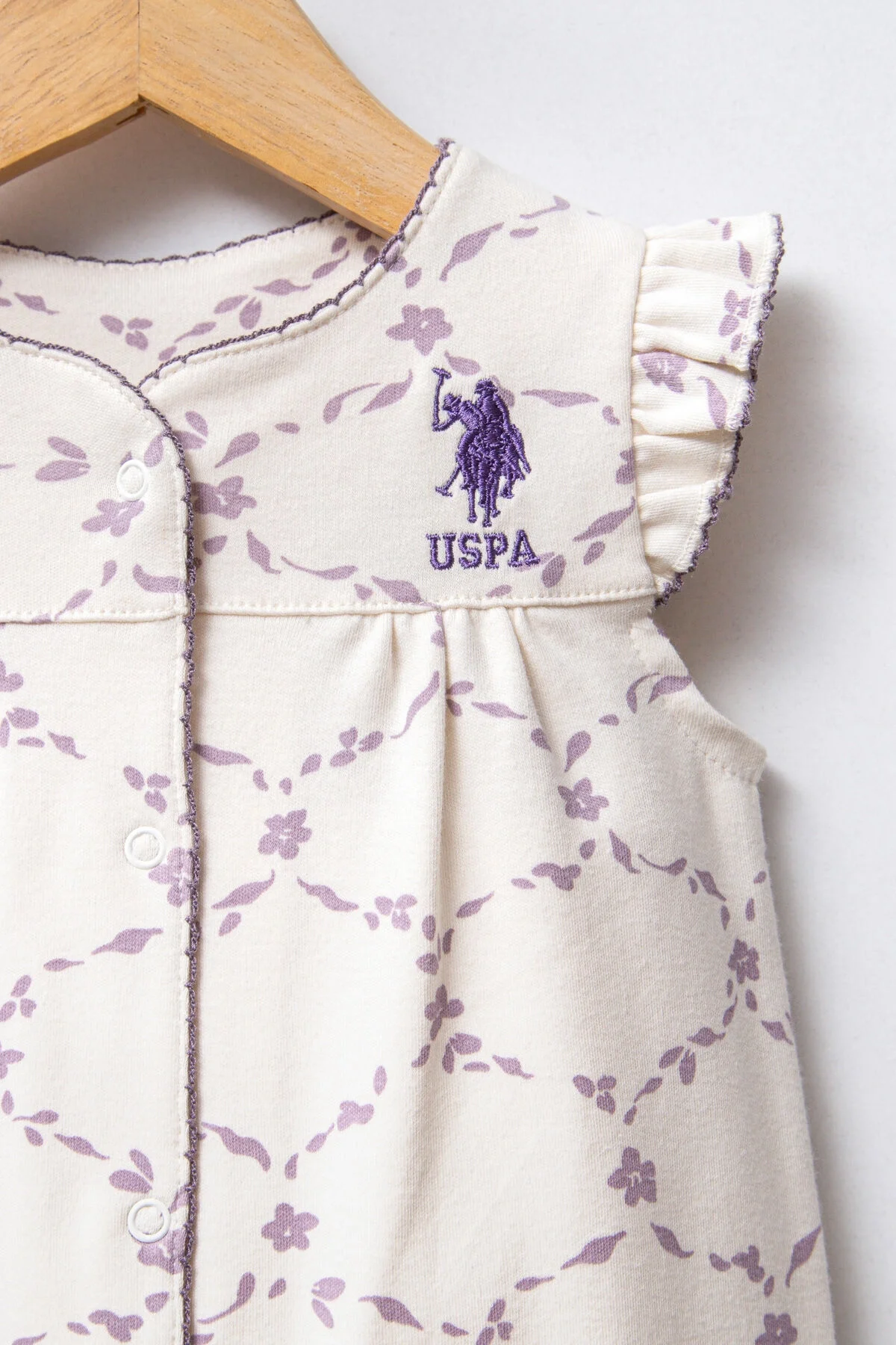 Beyaz desenli U.S. Polo Assn kız bebek tulumu, kolları olmayan, ön düğmeli, marka logosu ile detaylı ürün fotoğrafı