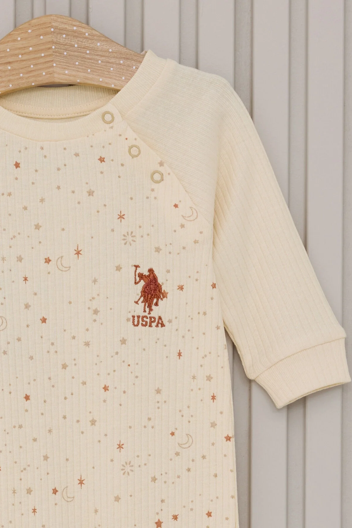 Krem renkli U.S. Polo Assn kız bebek tulum, yıldız ve ay desenli, ön göğüs üzerinde marka logosu, kolları ve bacakları düğmeli
