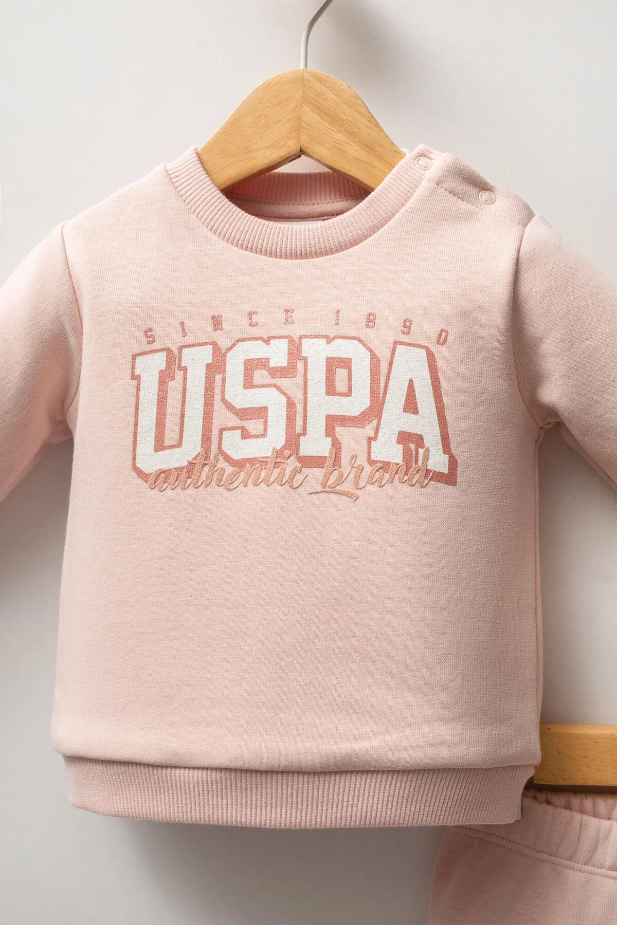 Pembe USPA marka kız bebek takım elbise, uzun kollu tişört ve pantolon, bebek giyim seti, marka logosu ile detaylı ürün görseli