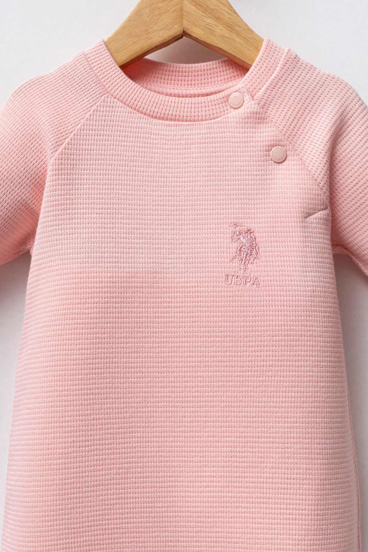 Pembe U.S. Polo Assn kız bebek tulumu, uzun kollu, düğme detaylı, ahşap asma üzerinde, bebek giyim kategorisi