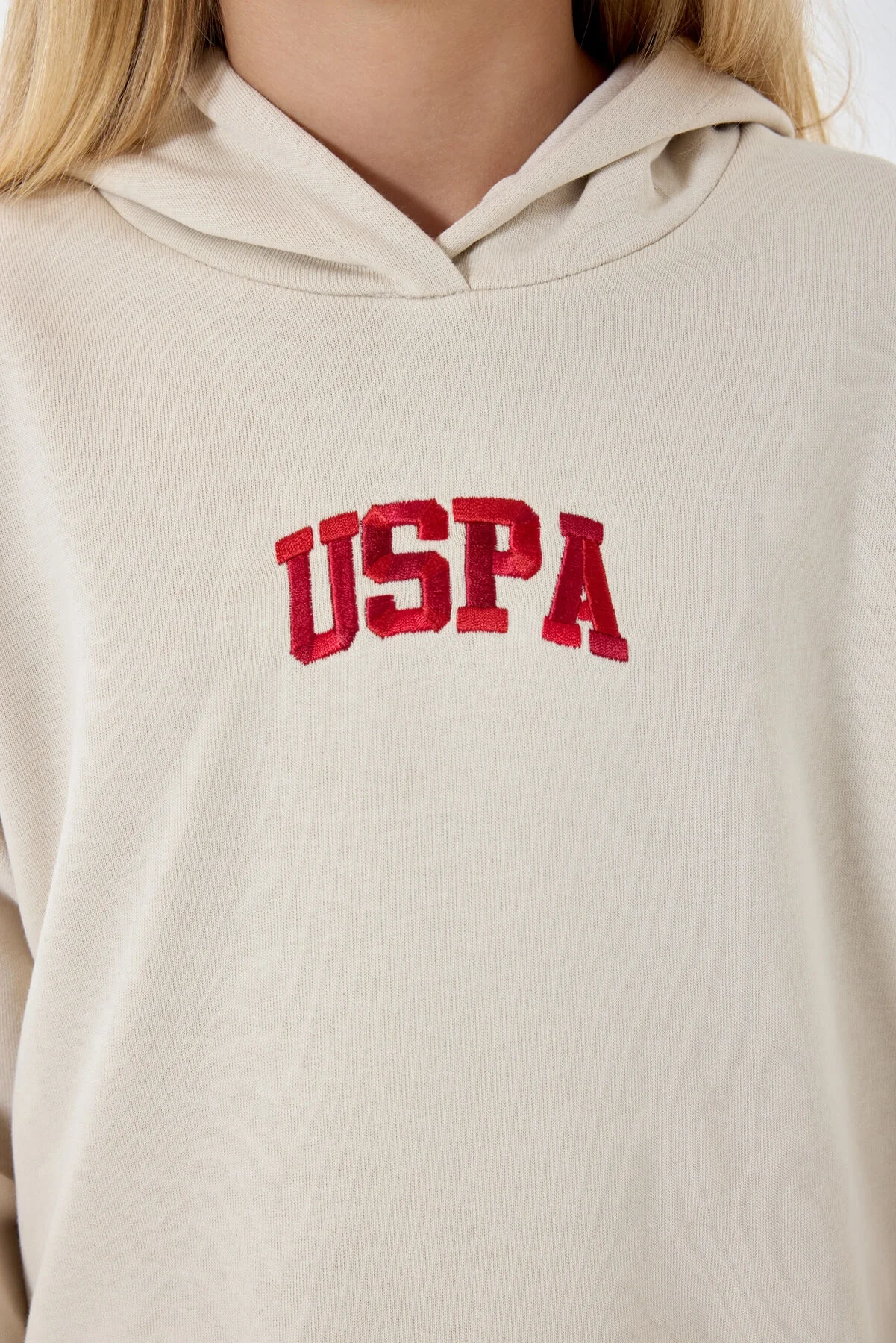 Krem renkli U.S. Polo Assn kız çocuk eşofman takımı, kapüşonlu üst ve pantolon, model pozisyonu, beyaz arka plan
