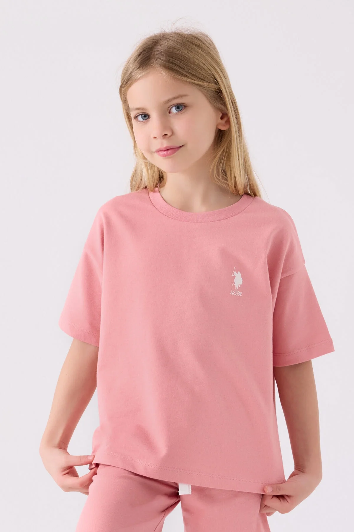 Pembe U.S. Polo Assn kız çocuk Bermuda takım seti, ön ve yan görünüm, marka logosu, beyaz spor ayakkabılarla搭配