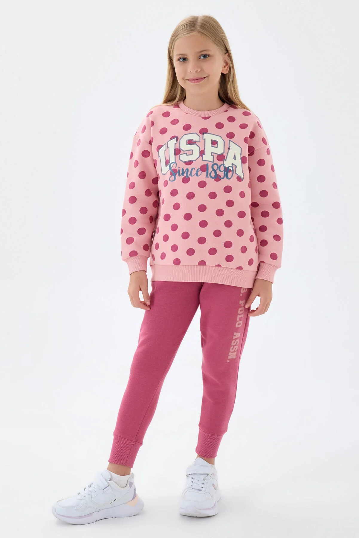 Pembe polka dot desenli U.S. Polo Assn kız çocuk eşofman takımı, model ön görünüm, spor stil, beyaz arka plan