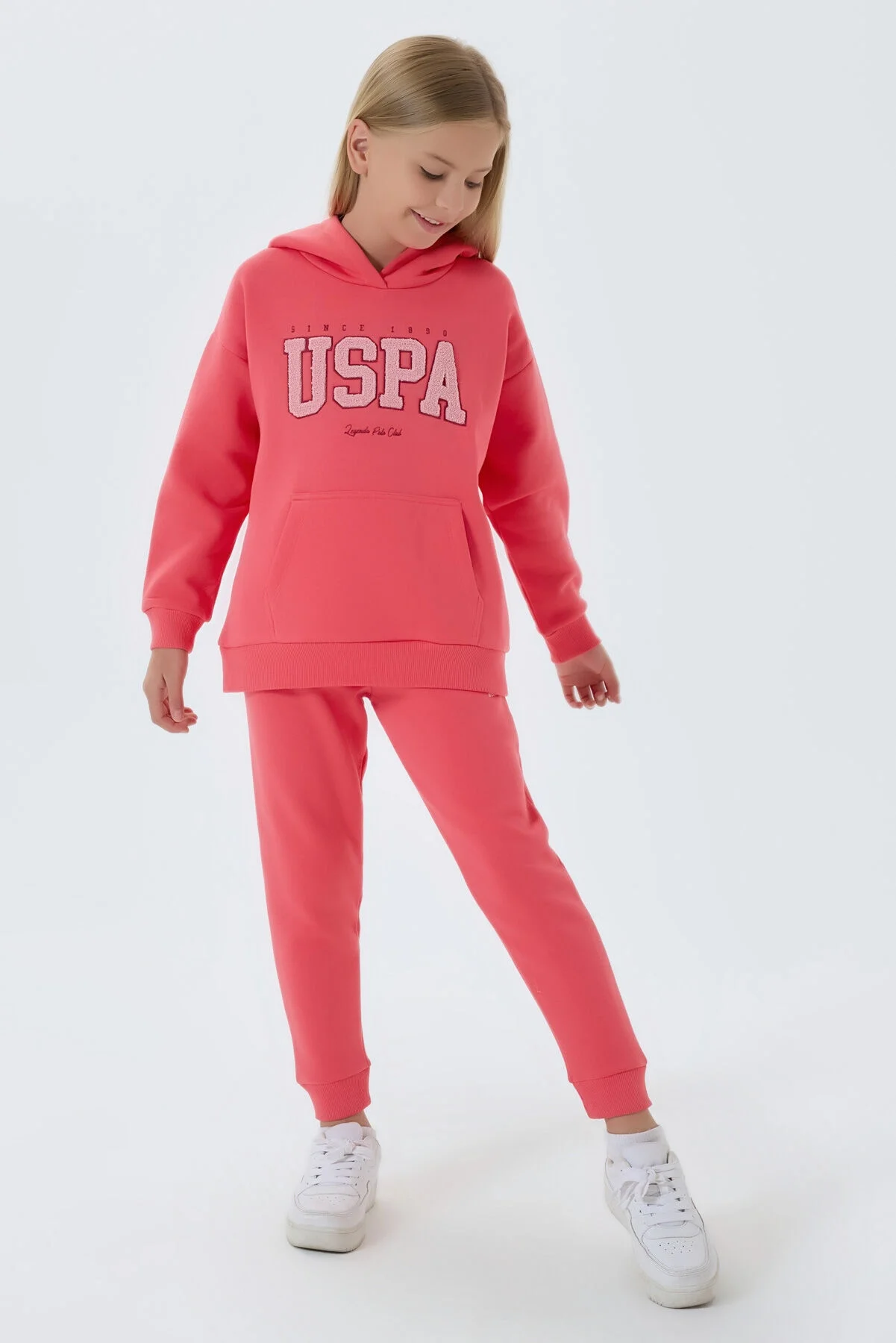 Pembe USPA marka kız çocuk eşofman takımı, kapüşonlu üst ve pantolon, spor stil, beyaz ayakkabılarla takımlı