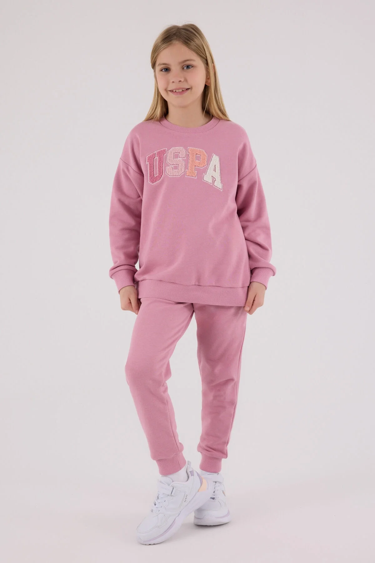 Pembe USPA markalı kız çocuk eşofman takımı, spor stili, ön görünüm, beyaz ayakkabılarla takımlı