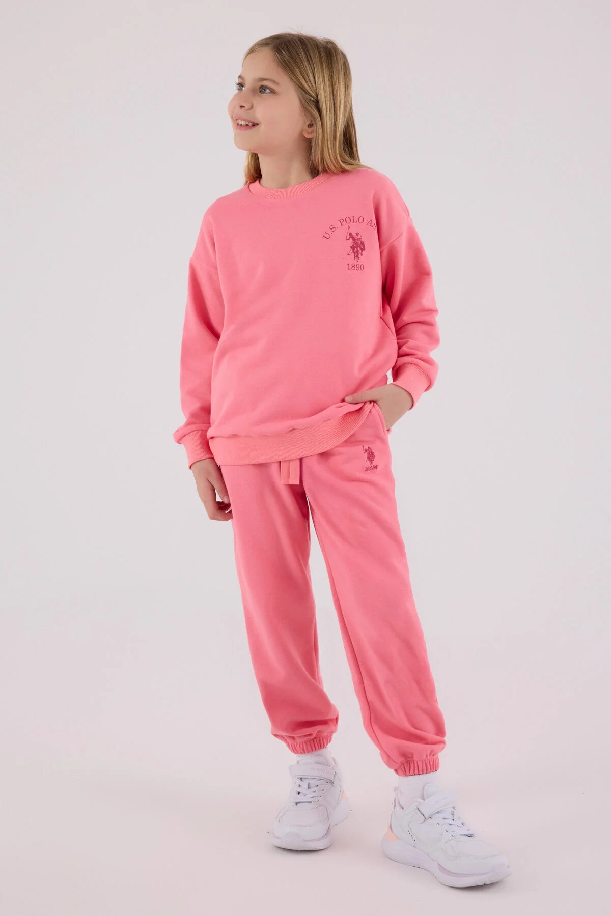 Pembe U.S. Polo Assn kız çocuk eşofman takımı, model ön görünüm, yumuşak kumaş, marka logosu, çocuk giyim