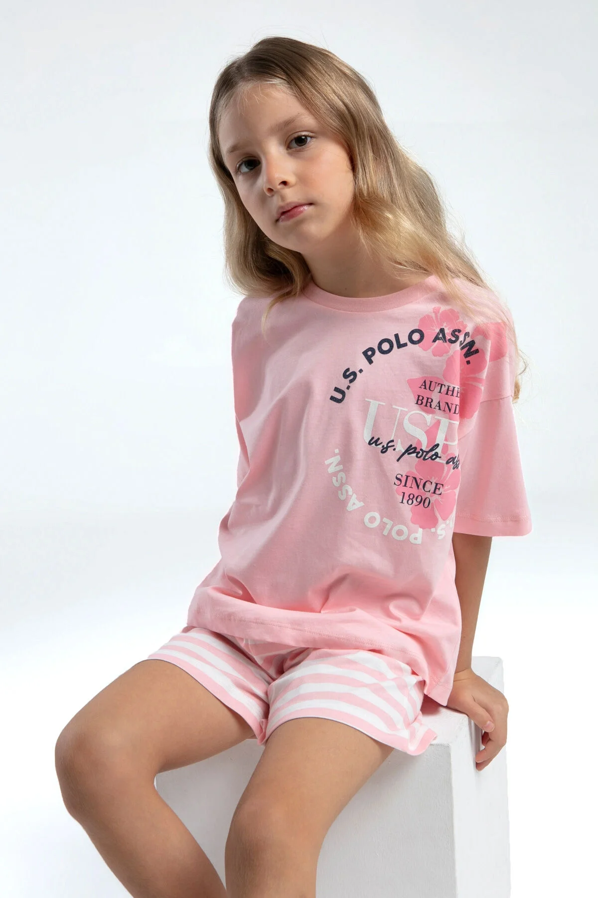 Pembe U.S. Polo Assn kız çocuk şort takım, üstte marka yazısı, altta pembe-beyaz çizgili şort, çocuk model ön görünüm