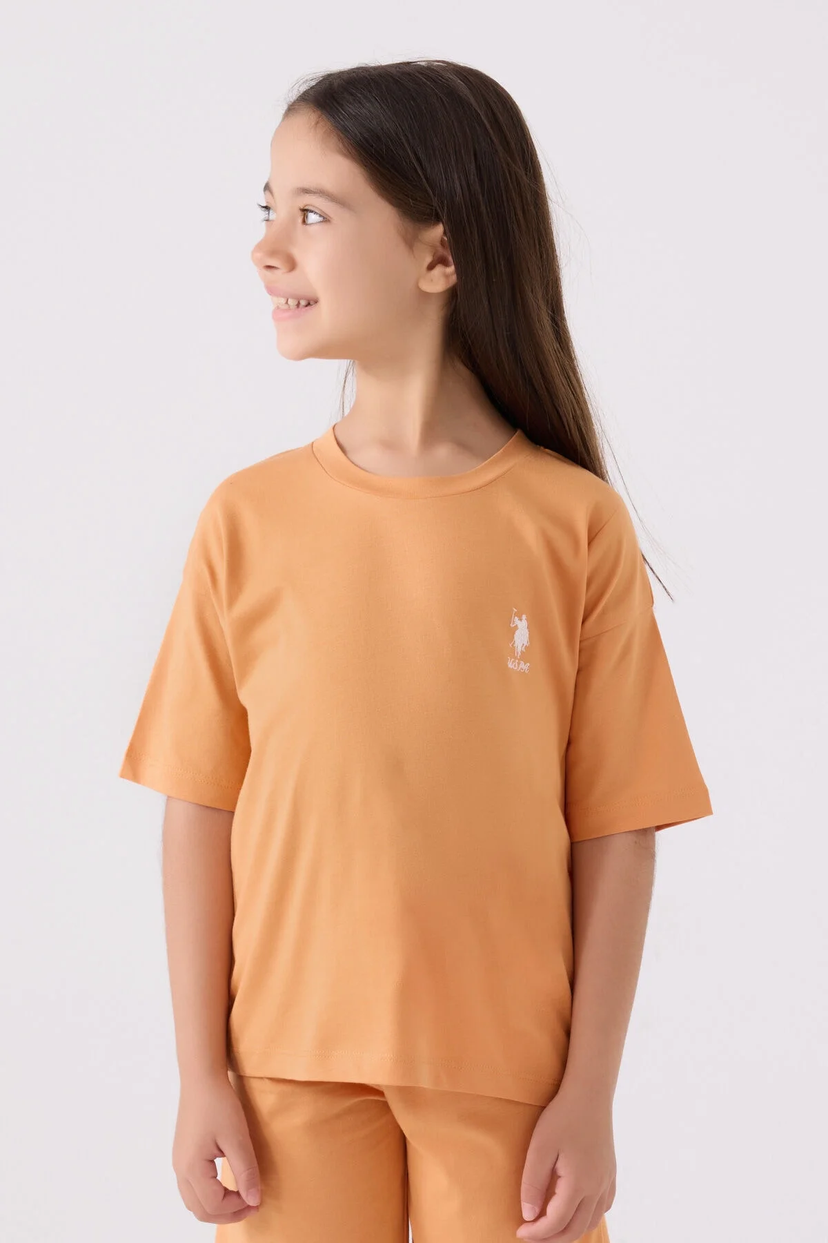 U.S. Polo Assn kız çocuk turuncu Bermuda takım seti, model ön görünüm, beyaz arka plan, marka logosu