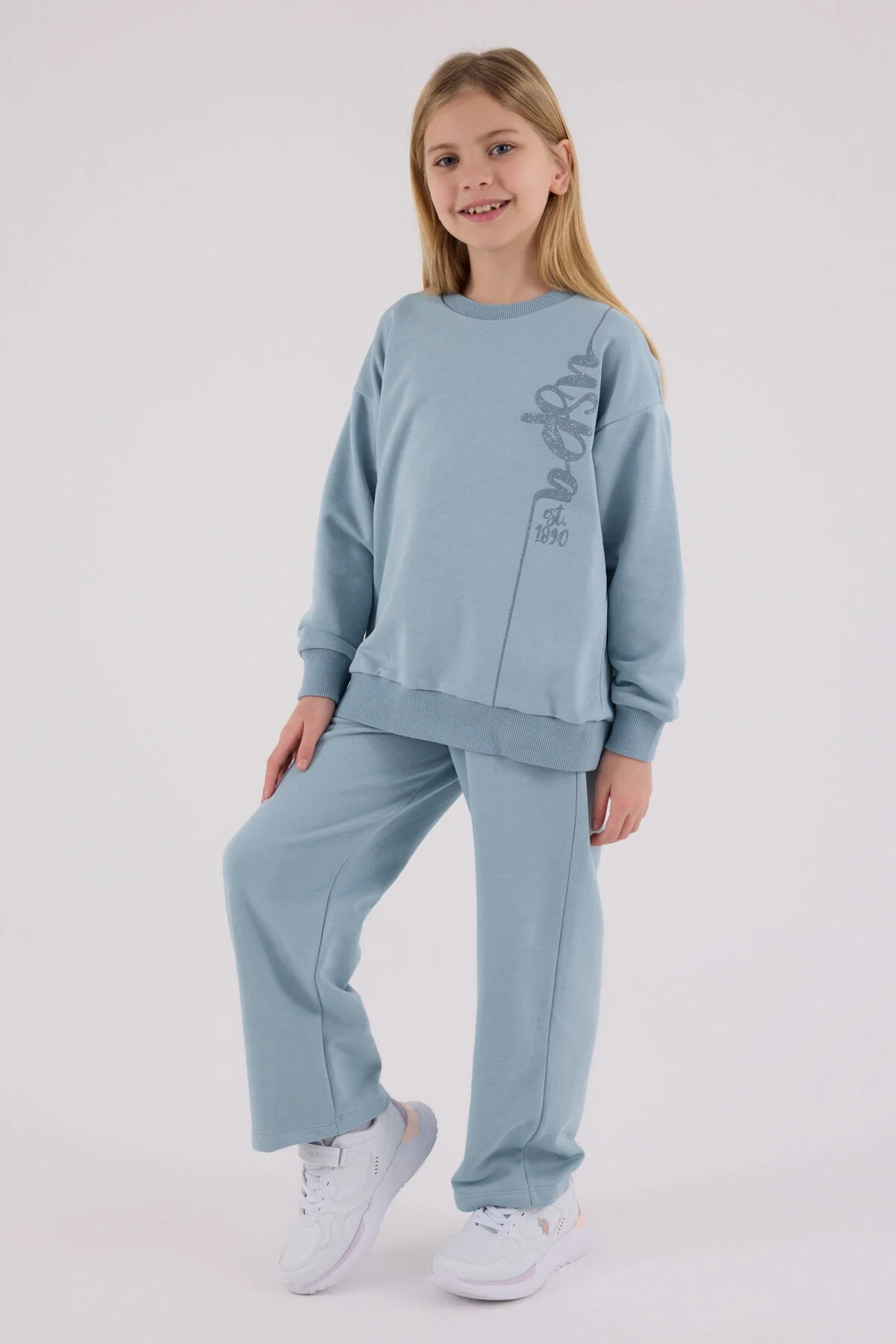 Mavi U.S. Polo Assn kız çocuk eşofman takımı, üstte yazı desenli, pantolonun ön cebinde marka logosu, model pozisyonu